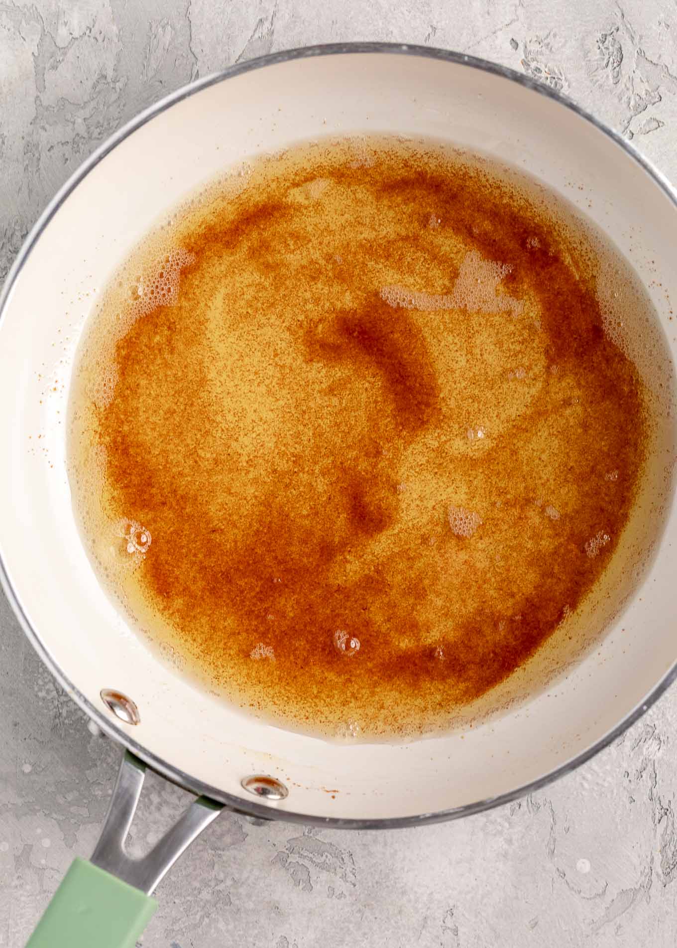 An overhead view of brown butter in a white skillet.