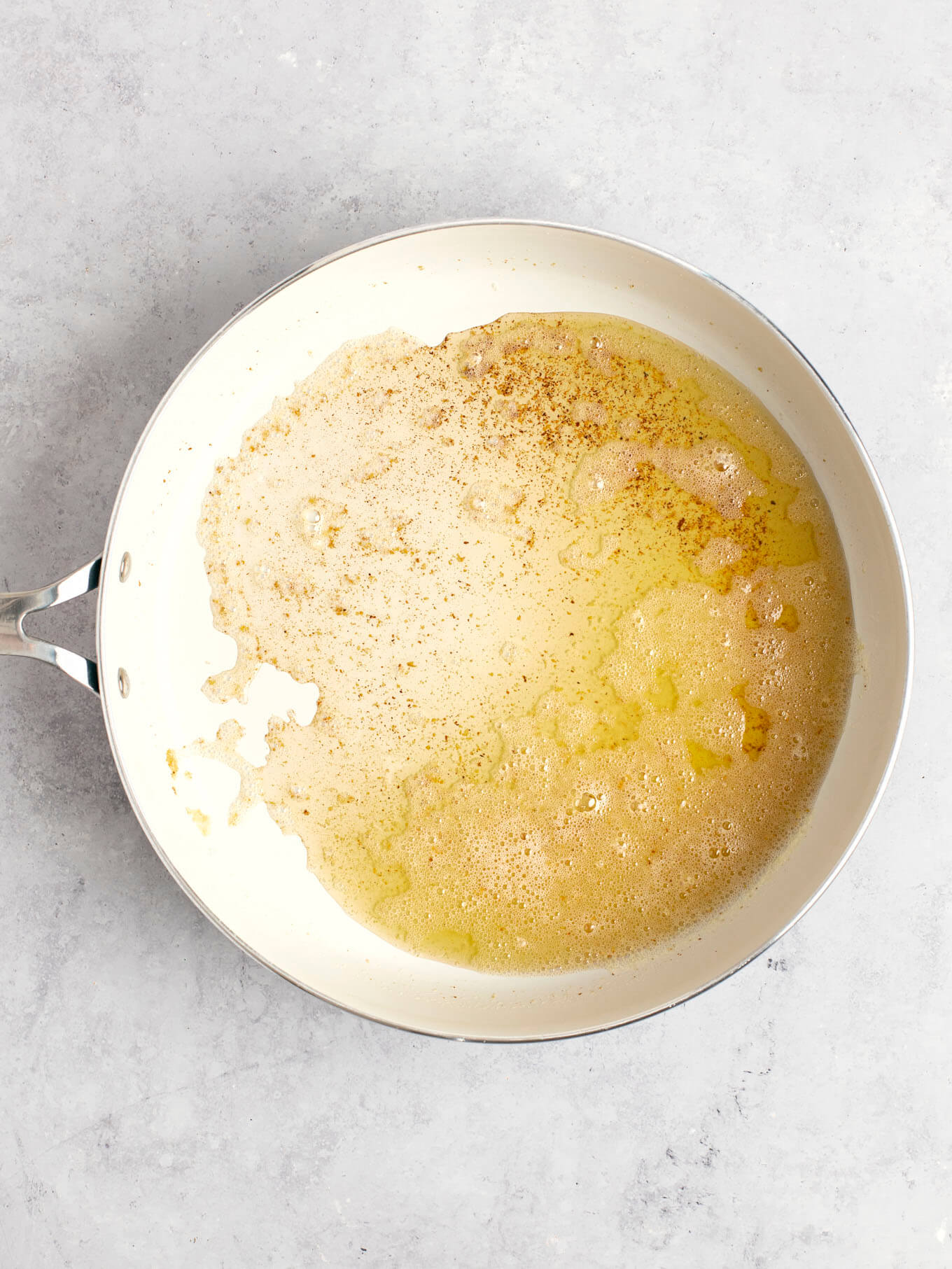 An overhead view of foamy butter with some browned bits in the bottom of the skillet.