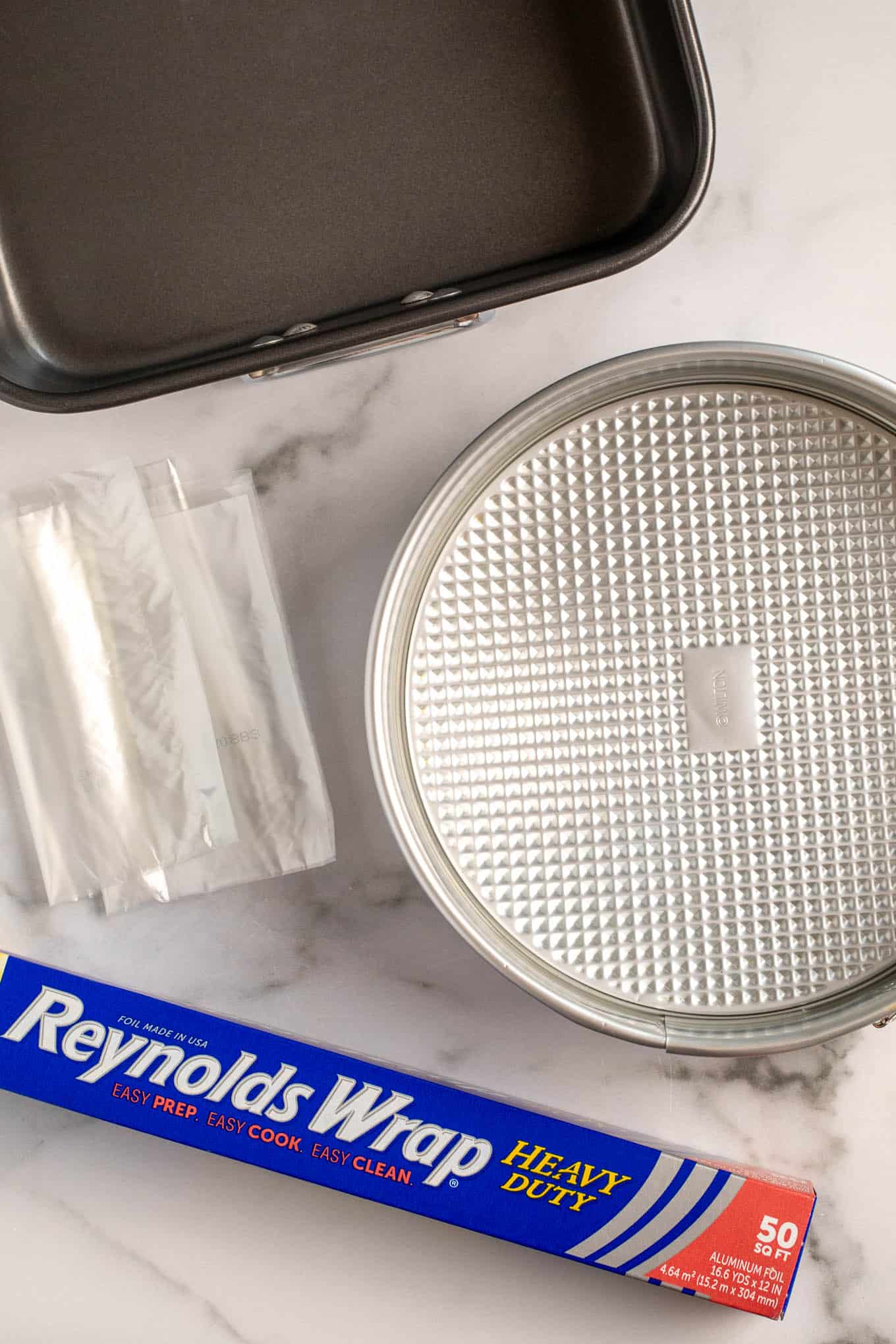 An overhead view of a large roasting pan, an oven bag, a springform pan, and aluminum foil.