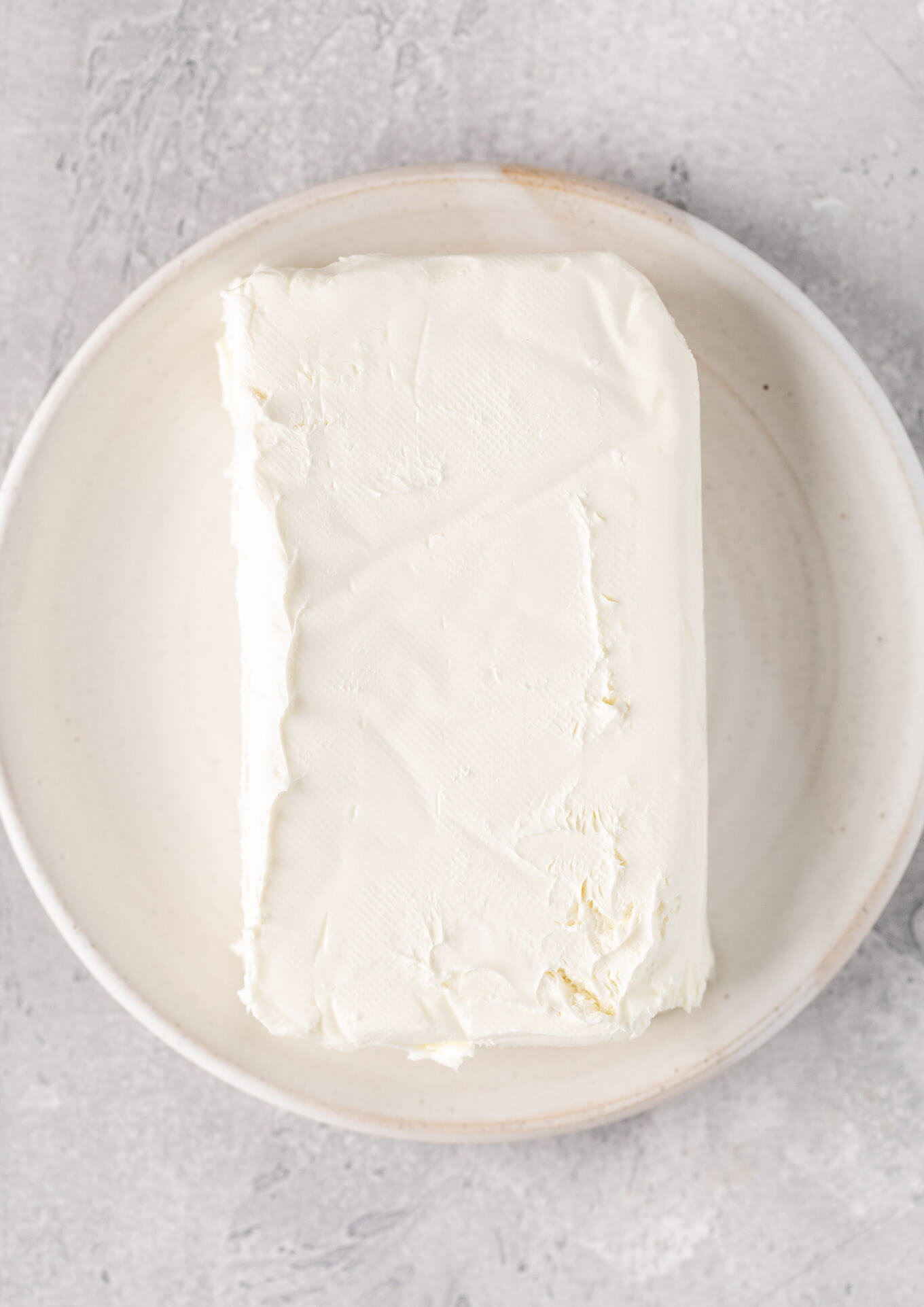 An overhead view of a block of cream cheese on a white plate.