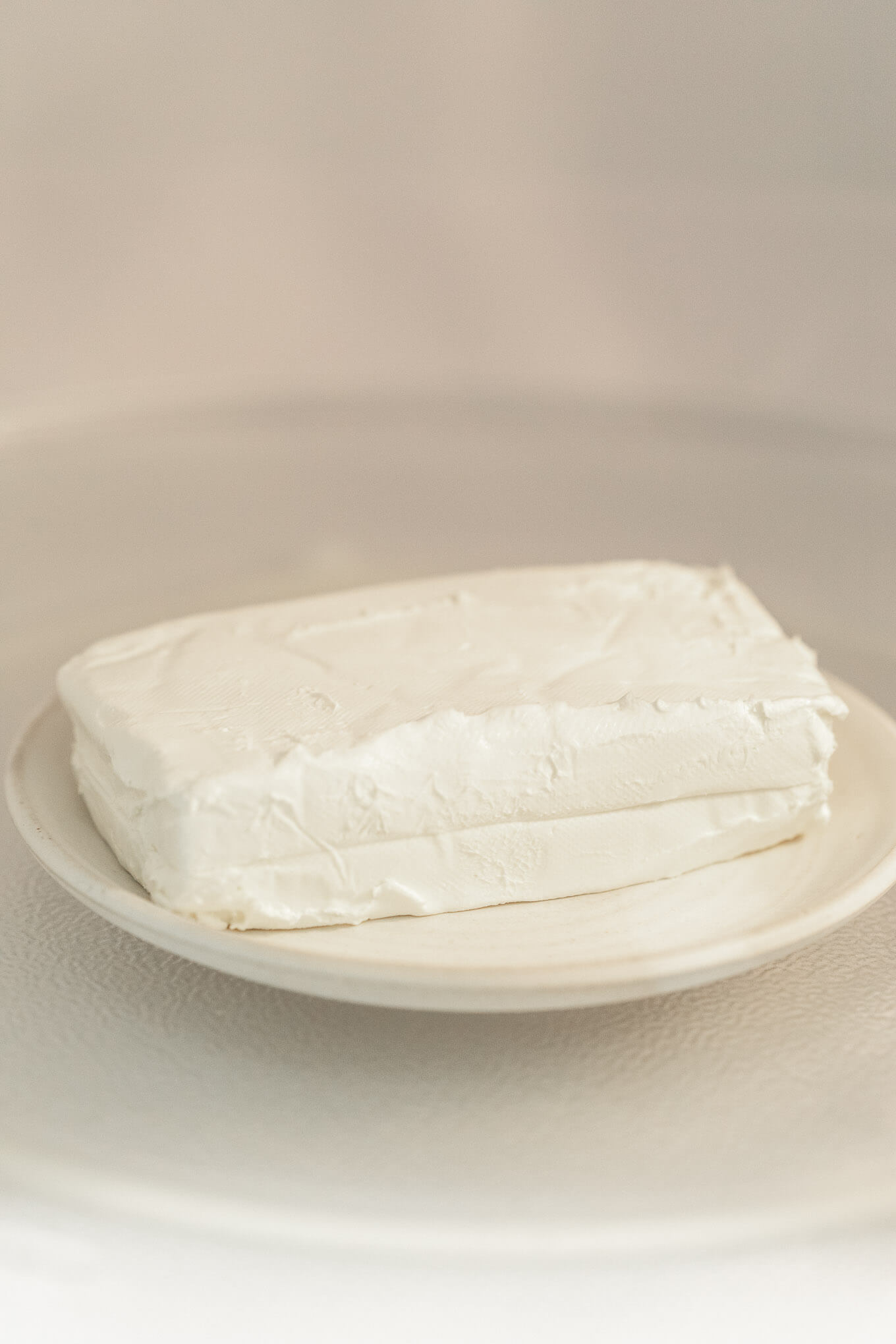 A plate with a block of cream cheese sitting inside of a microwave. 