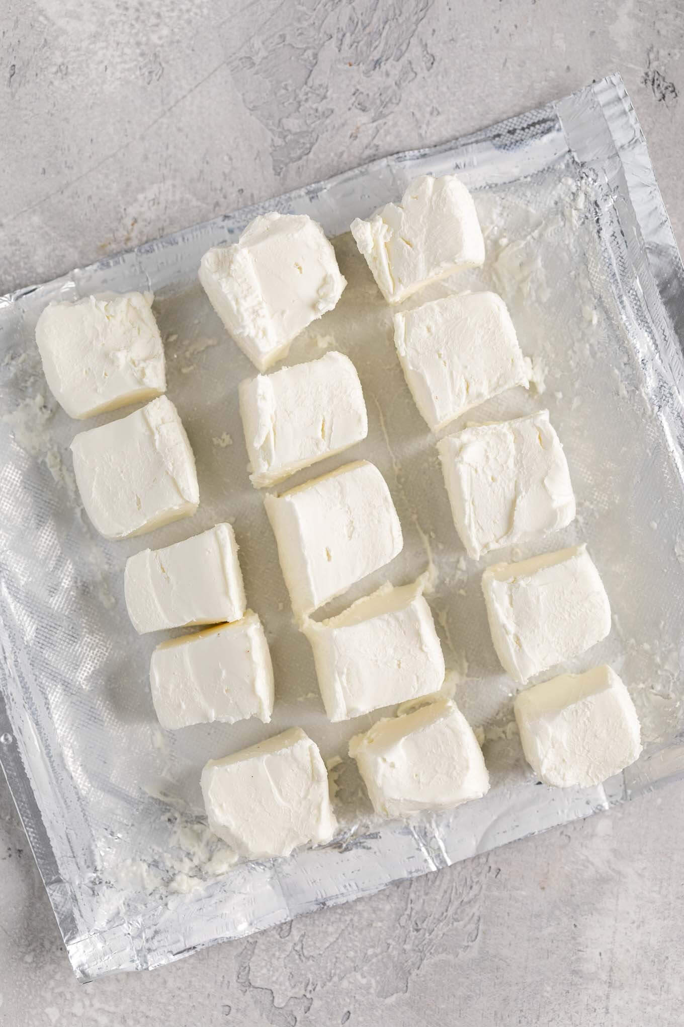 An overhead view of an opened package of cream cheese that's been cubed into several small pieces.