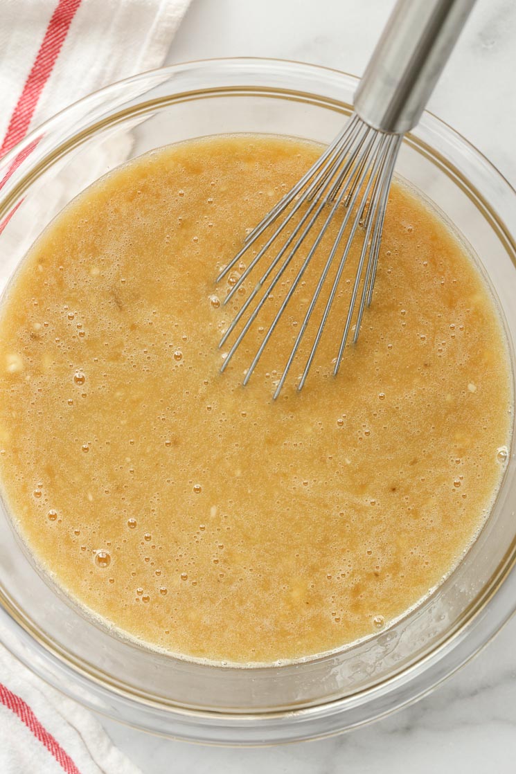 A glass bowl filled with the wet ingredients for a cake and a metal whisk.