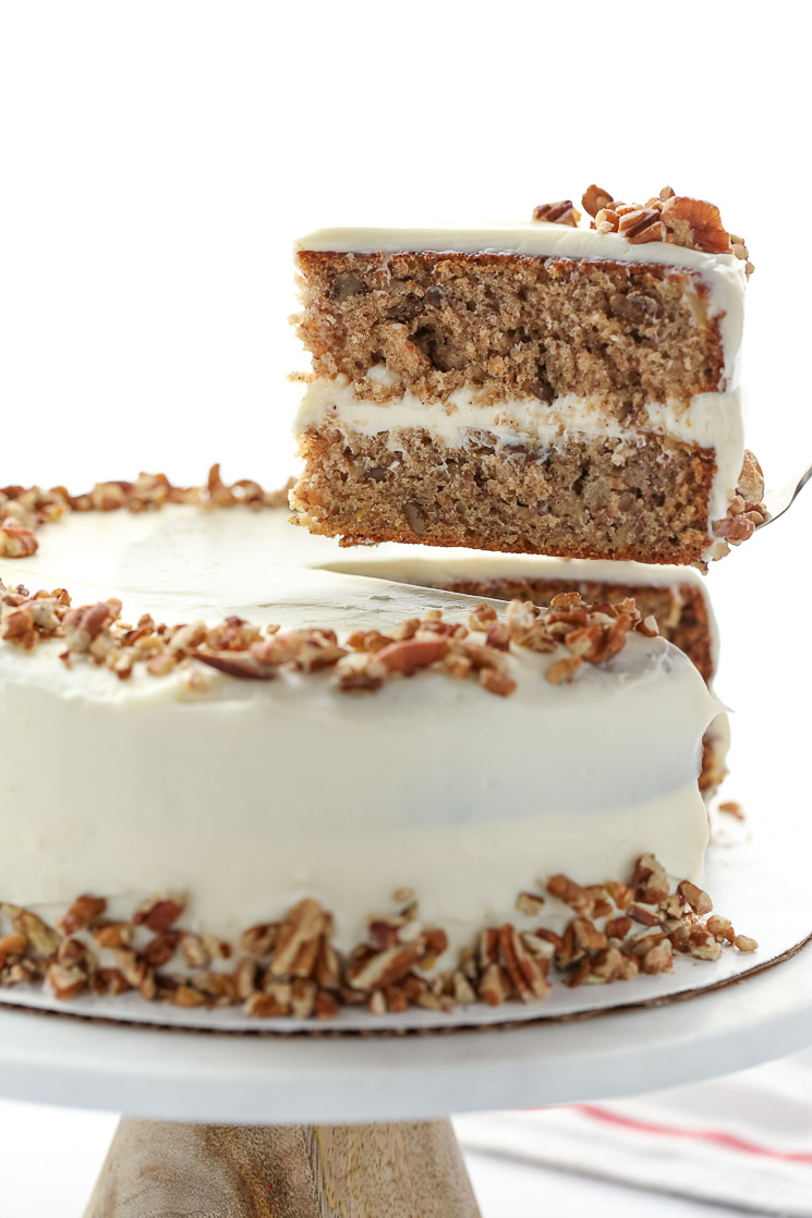 A whole hummingbird cake on top of a marble cake stand with one piece being removed to show the cake layers. 