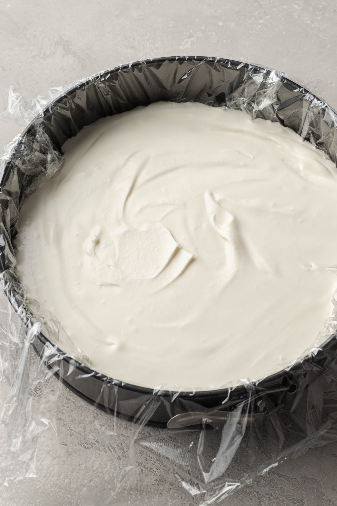 Vanilla ice cream spread out into a springform pan that's been lined with plastic wrap.