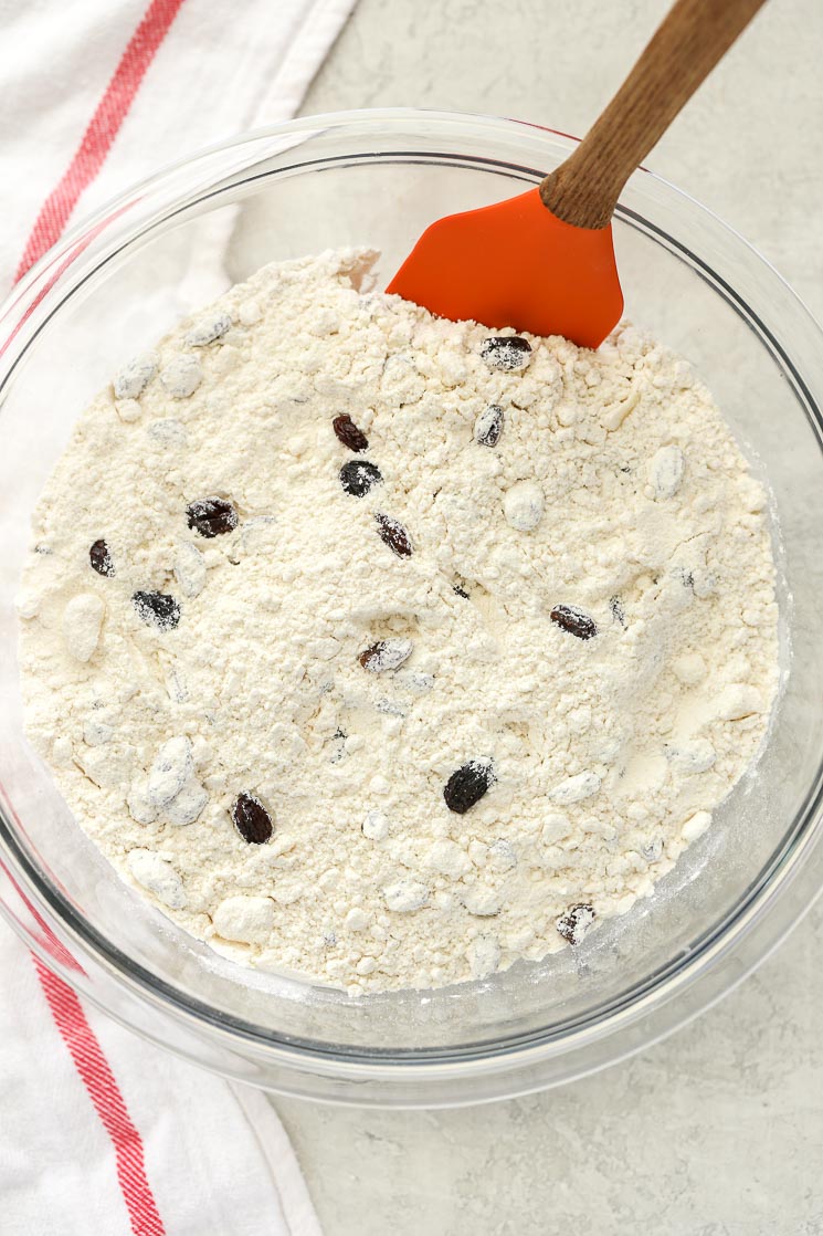 A clear glass bowl filled with the dry ingredients for Irish Soda Bread sitting on top of a white and red napkin. 