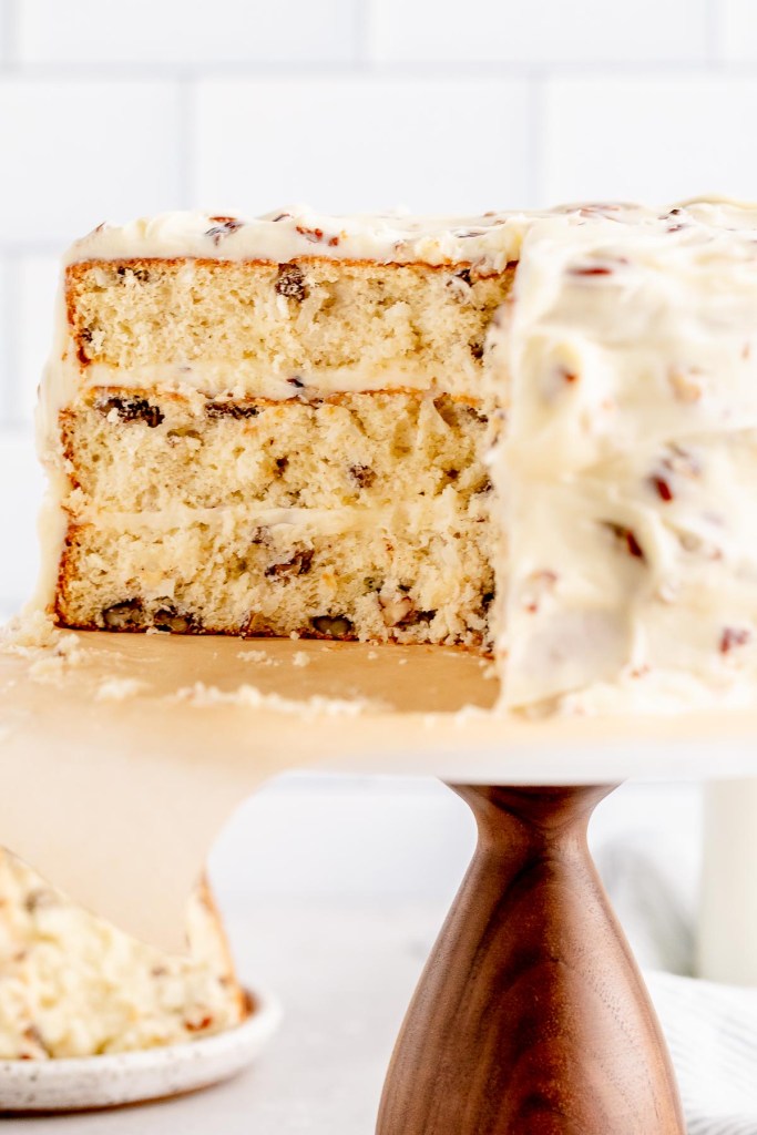 A close-up of an Italian Cream cake that's been sliced to show the texture. A slice of cake and a jug of milk rest in the background.