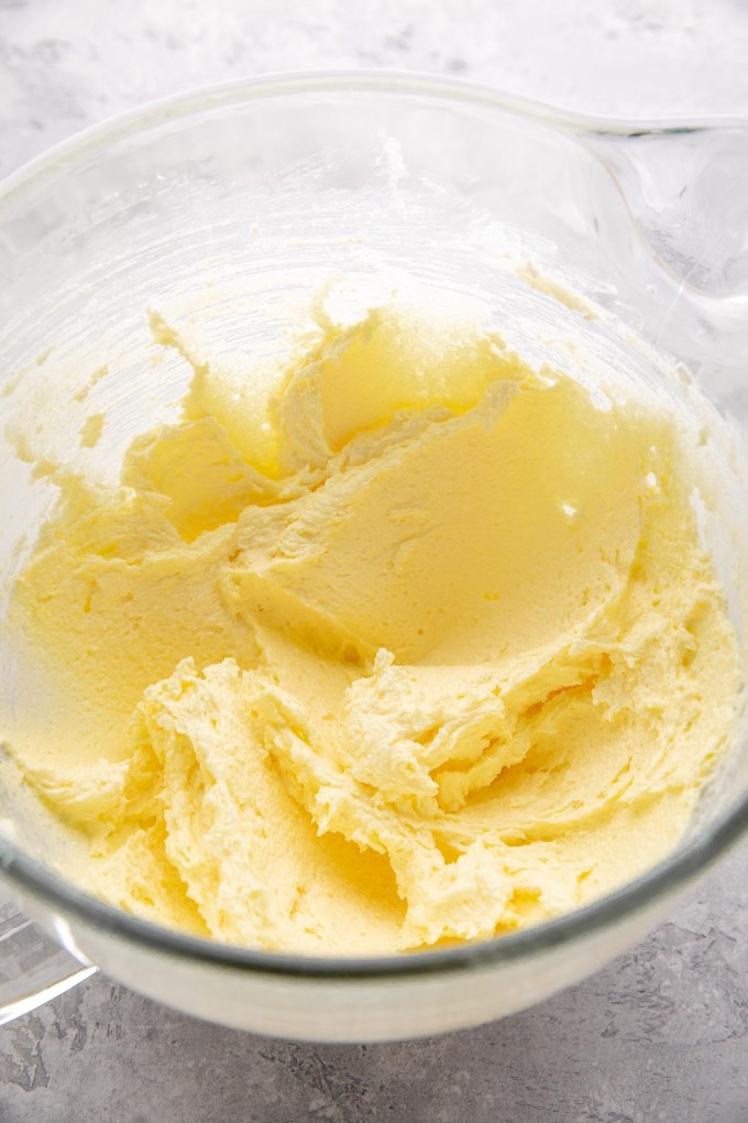 Butter, sugar, and egg yolks mixed together in a large glass mixing bowl.