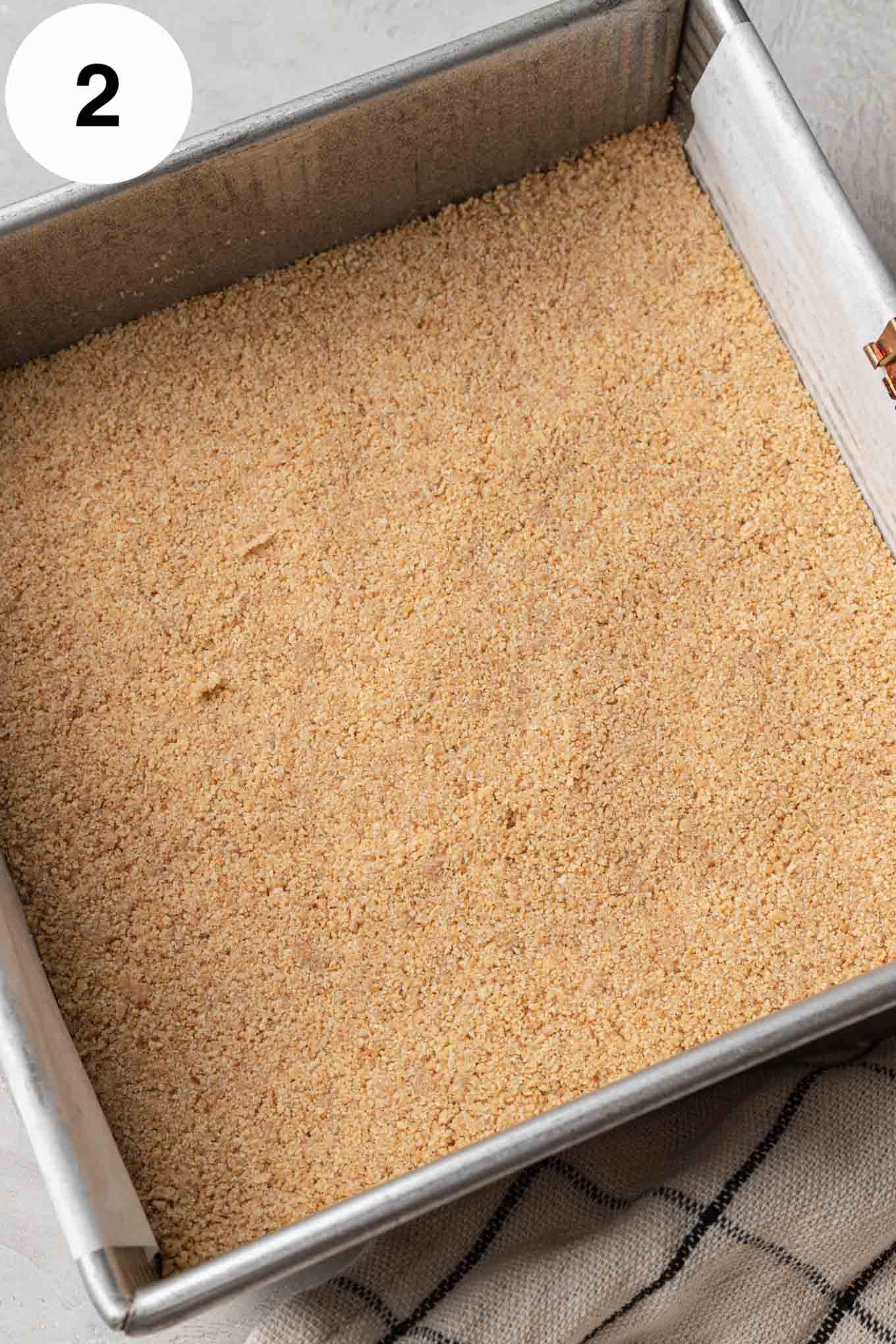 A graham cracker crust pressed into an 8-inch square baking pan lined with parchment paper.