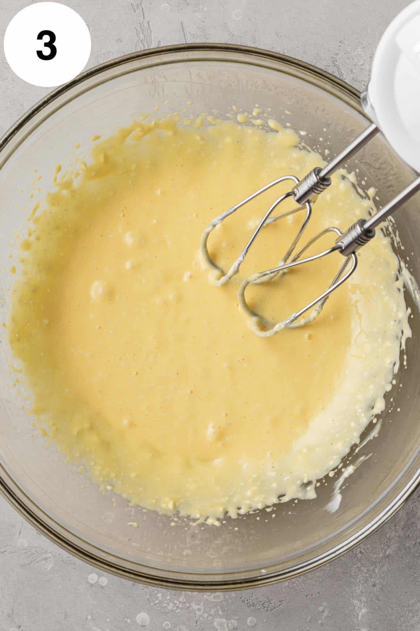 An overhead view of a cream cheese-egg mixture in a glass mixing bowl. 