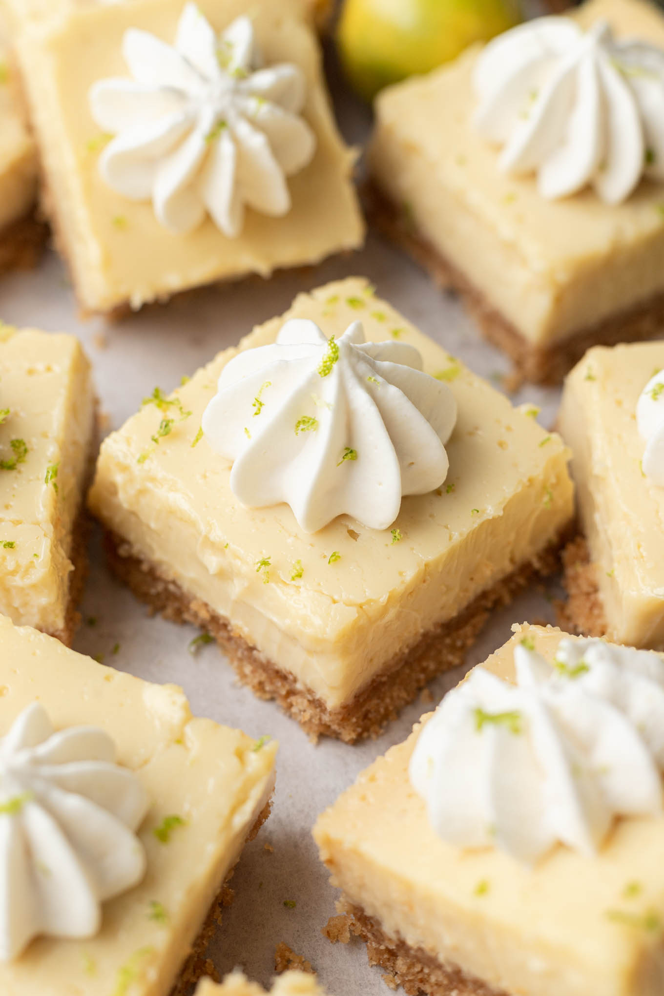 Sliced key lime pie bars garnished with lime zest and dollops of whipped cream. 