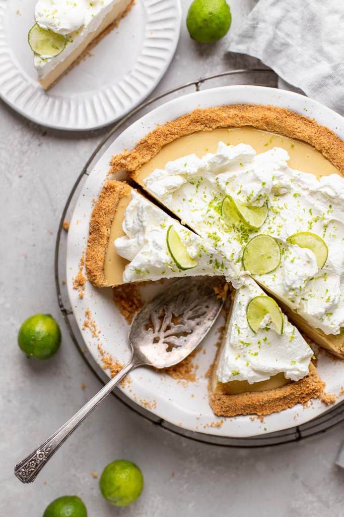 An overhead view of a key lime pie on a white plate, with one slice missing and two more slices cut out. 