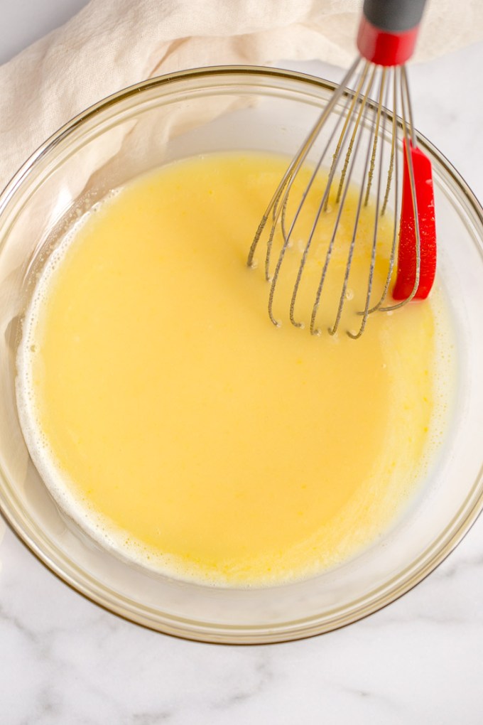 The lemon filling inside of a glass bowl with a whisk on the side.