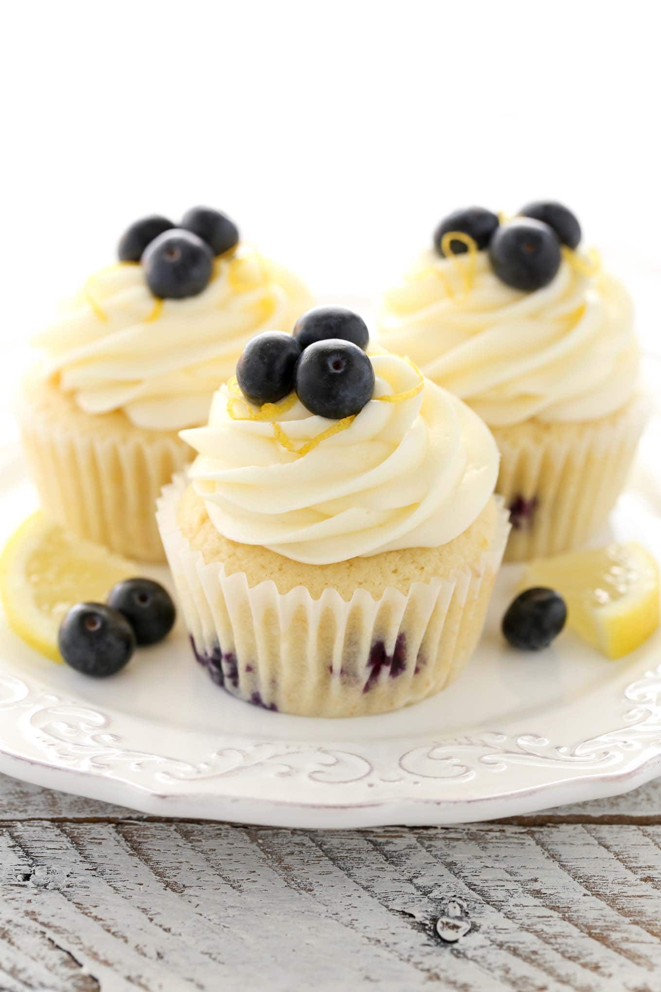 Three lemon blueberry cupcakes topped with lemon frosting on a white dessert plate. 