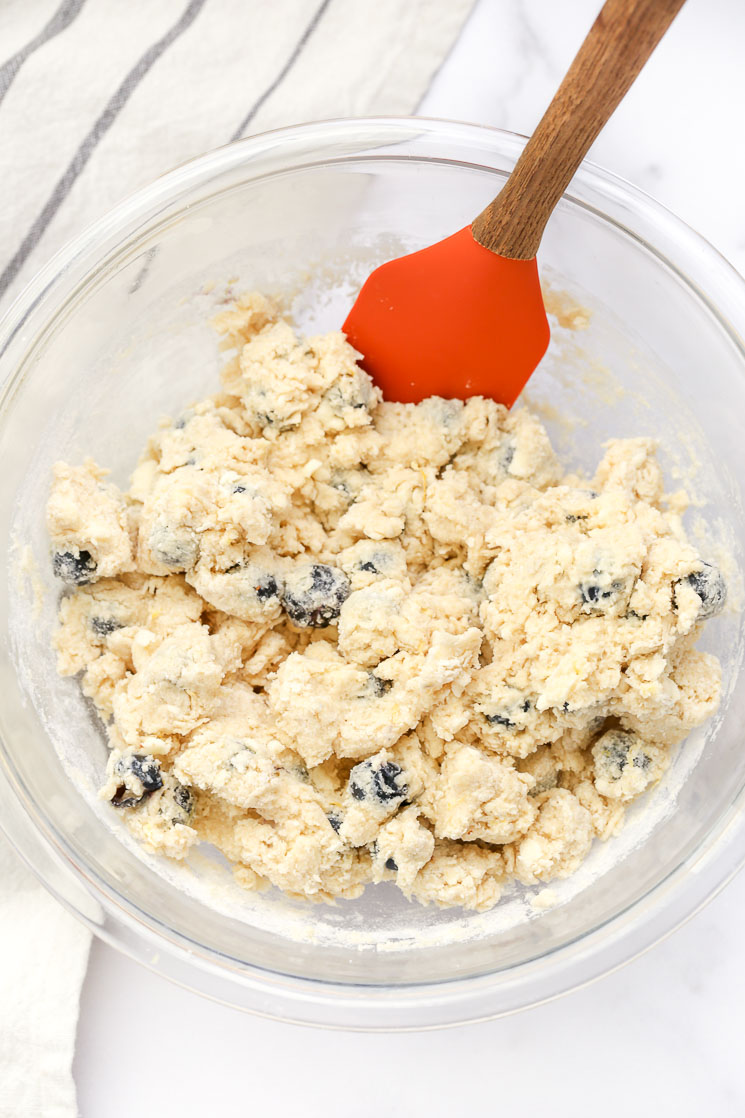 A large glass bowl filled with the dough for lemon blueberry scones and a rubber spatula on the side.