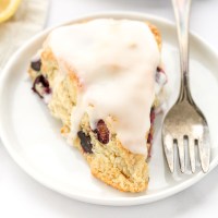 A closeup shot of a lemon blueberry scone on a white plate with a fork on the side.