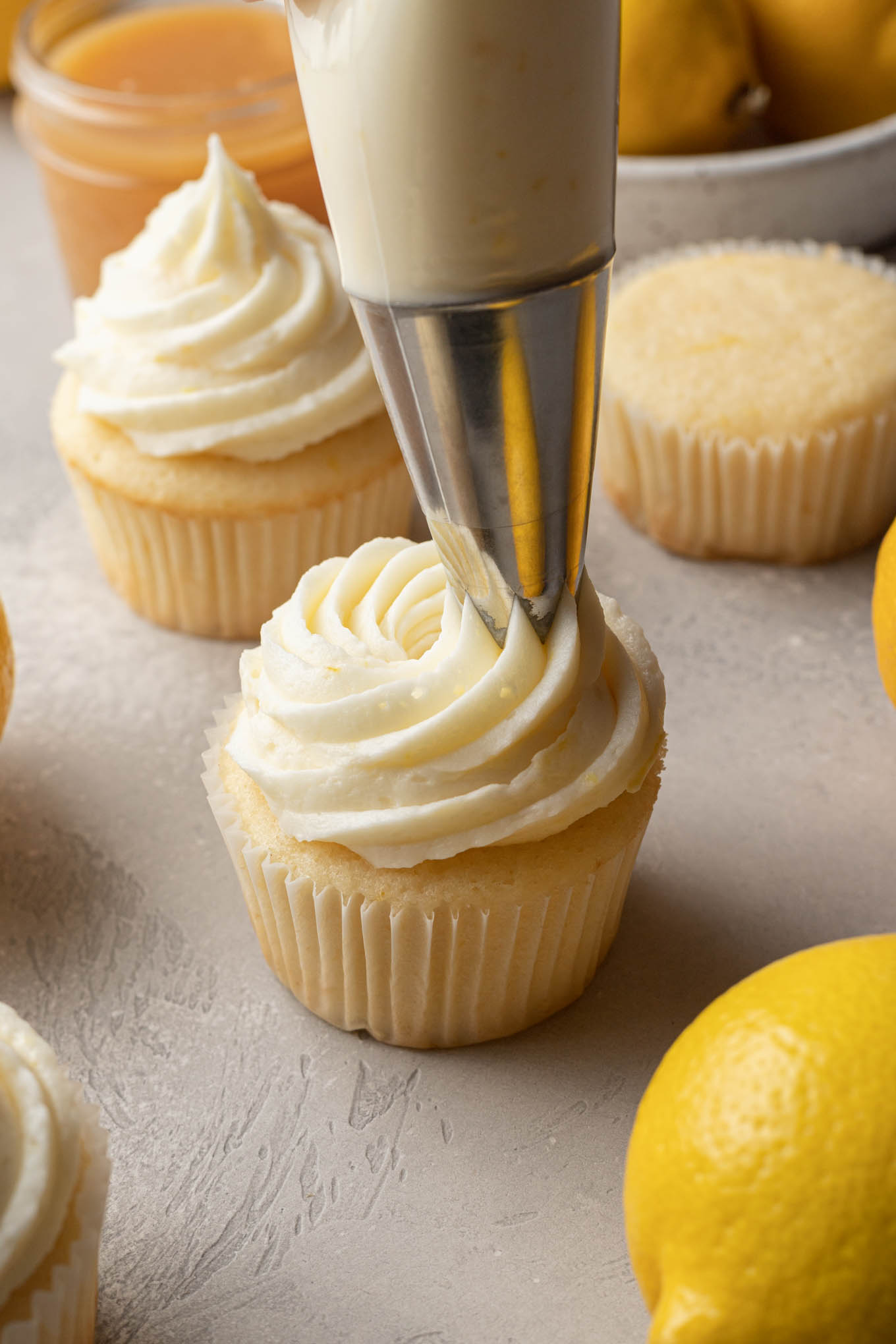 A process shot showing lemon buttercream being piped atop a cupcake. 