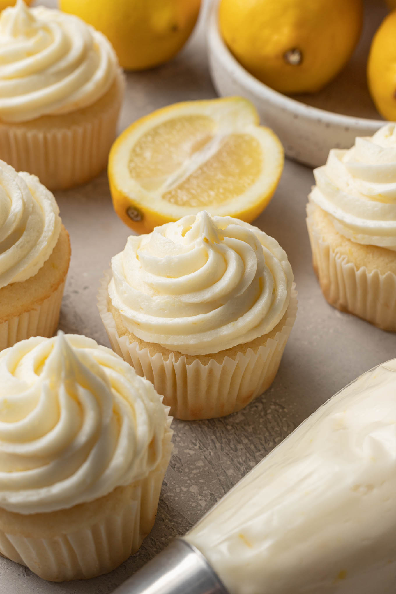 Cupcakes frosted with lemon buttercream, next to a dish of lemons. 