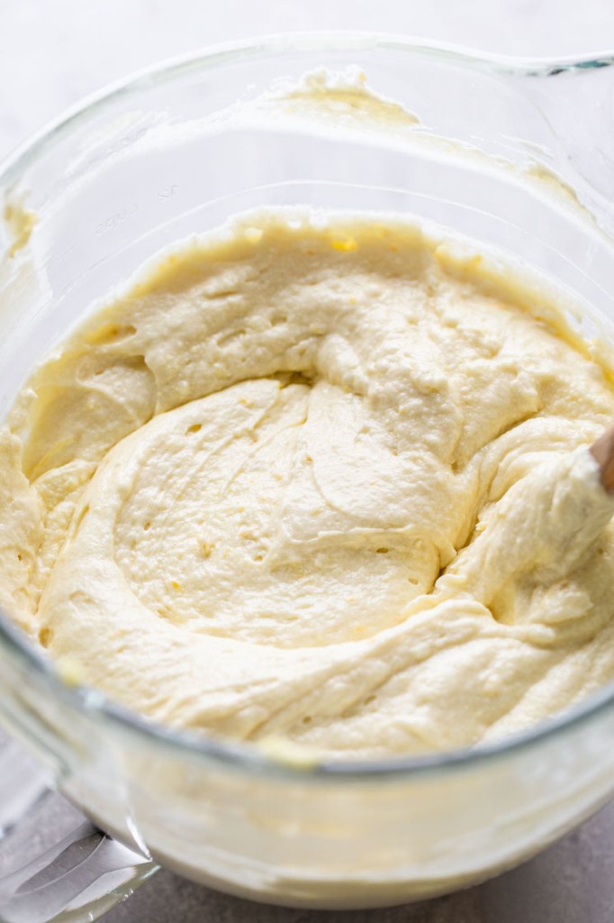 Homemade lemon cake batter in a glass mixing bowl. A wooden spoon rests in the bowl. 