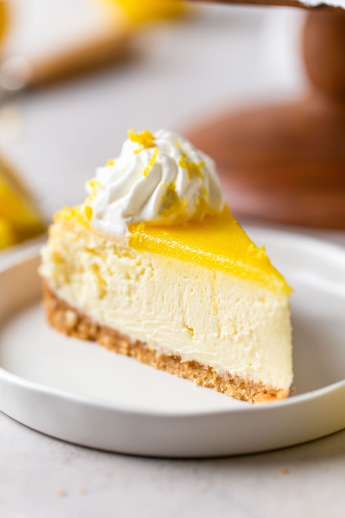 A slice of lemon cheesecake topped with lemon curd on a white dessert plate. 