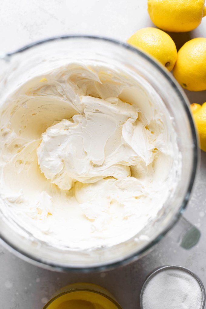 An overhead view of a glass mixing bowl filling with beaten cream cheese.