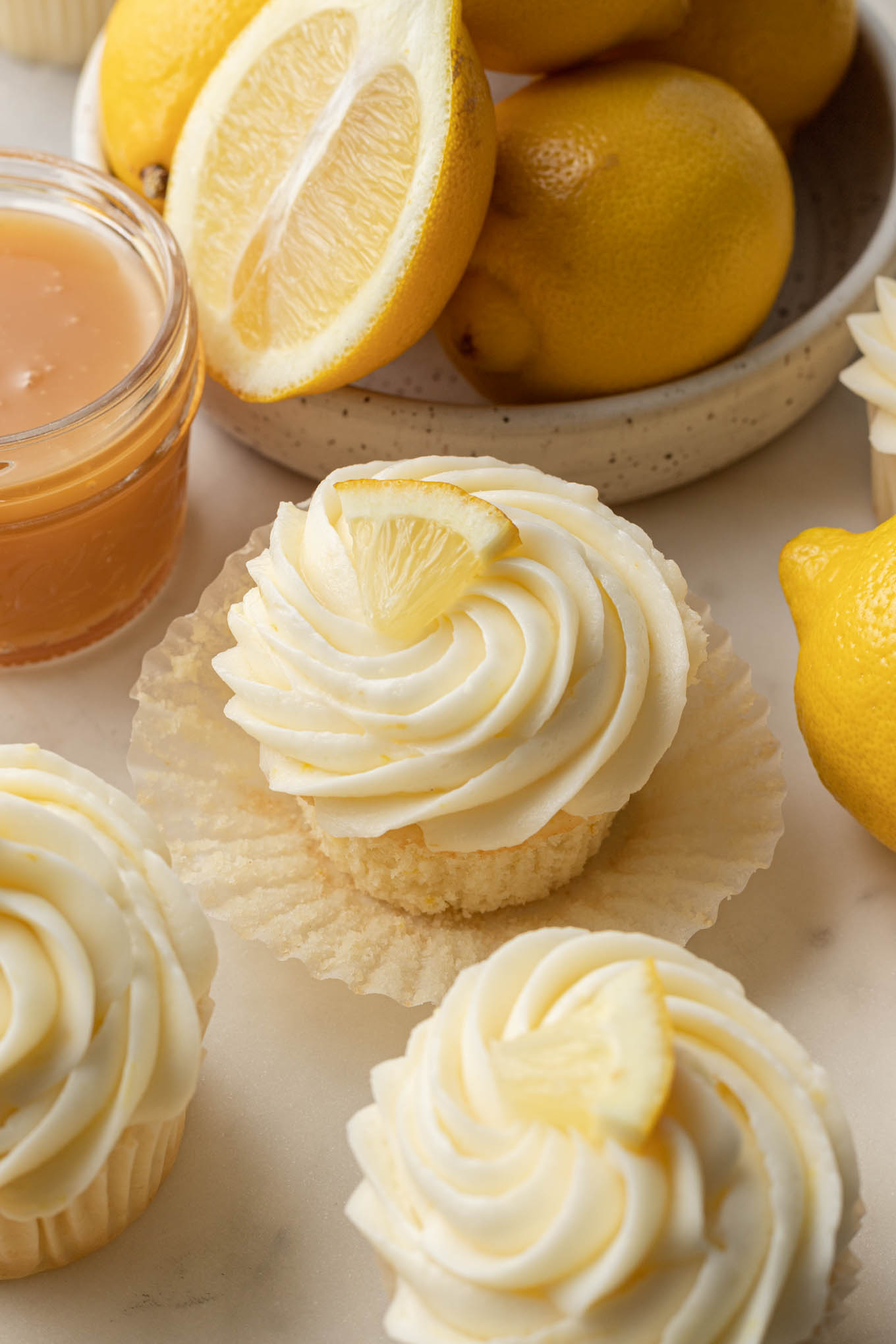 Lemon cupcakes in cupcake liners, surrounded by fresh lemons. 