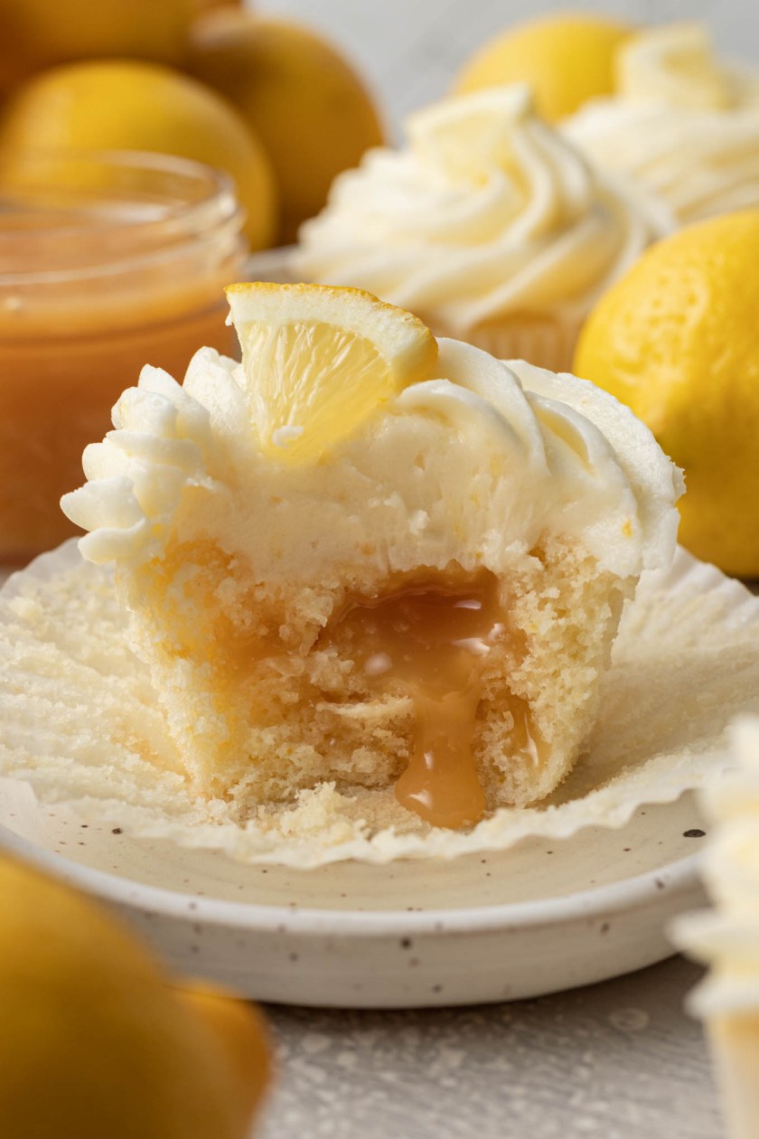 A close up view of a lemon curd filled cupcake with a bite missing. The lemon curd is oozing out of the cupcake. 