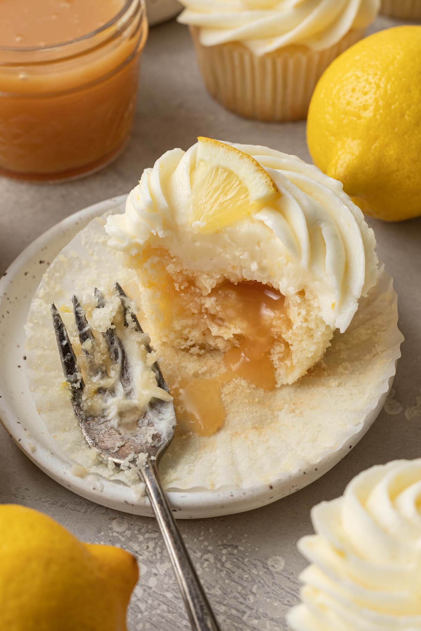 A lemon curd cupcake on a dessert plate, with a piece missing. The lemon curd is oozing out. 