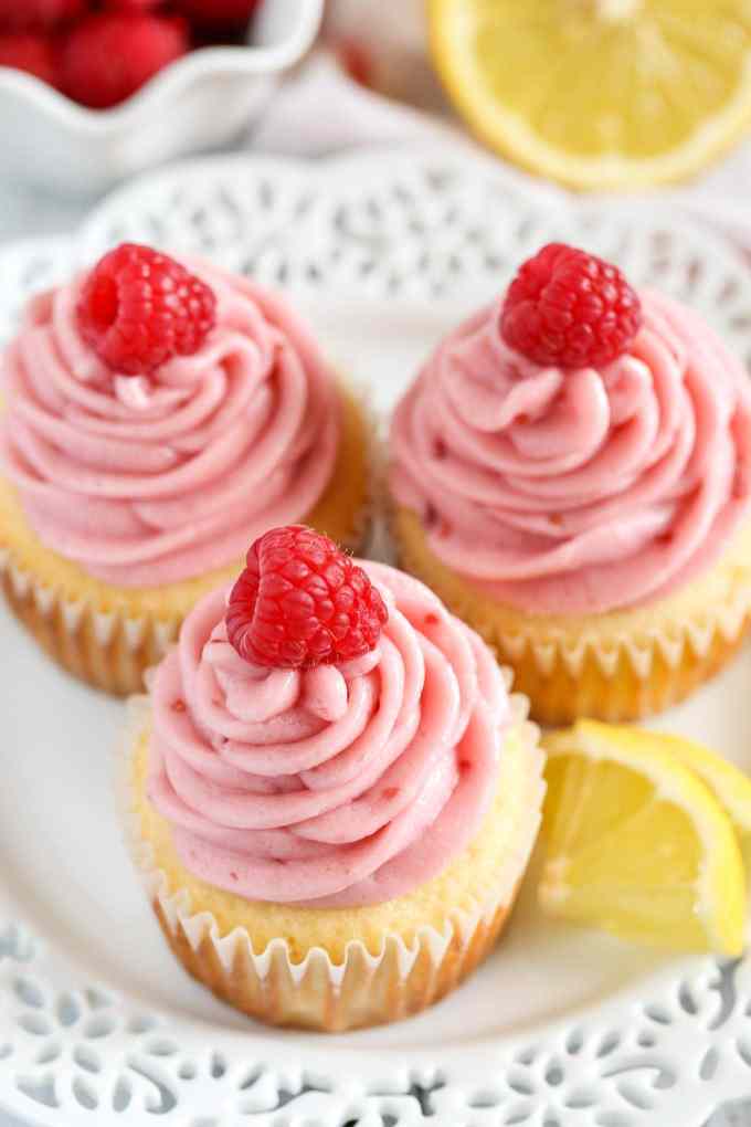 Top view of lemon cupcakes topped with raspberry buttercream and fresh raspberries on a white plate. 