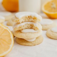 A stack of three lemon meltaway cookies topped with lemon icing. The top cookie is broken in half.