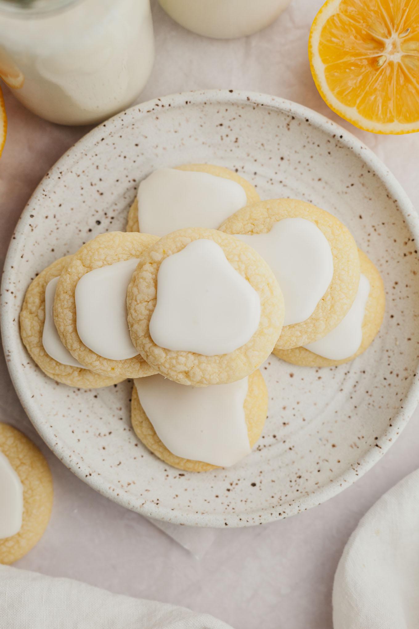 An overhead view of a stack of lemon meltaway cookies with icing on a white speckled plate. 