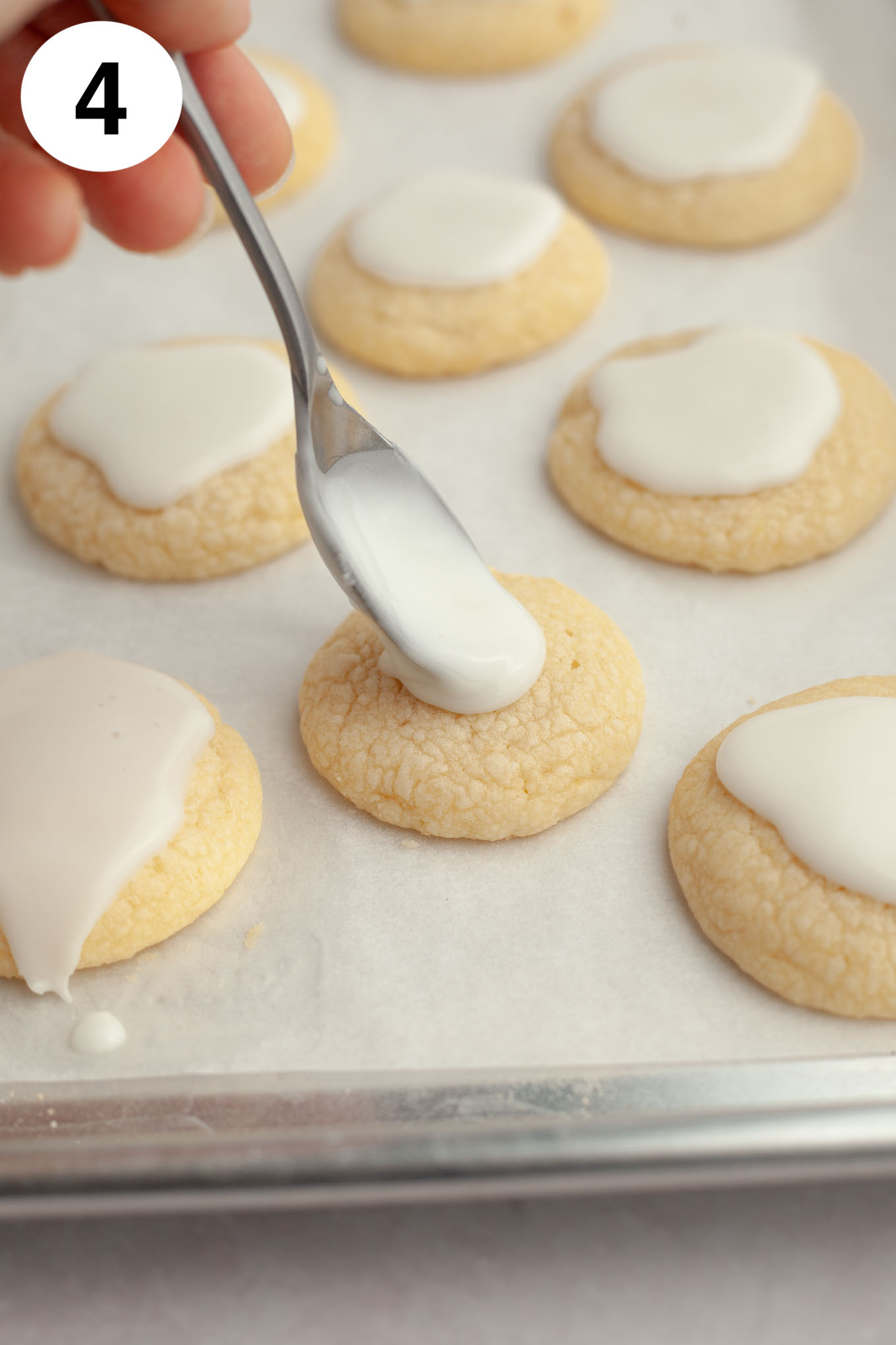 A process shot showing lemon icing being drizzled over soft lemon cookies. 