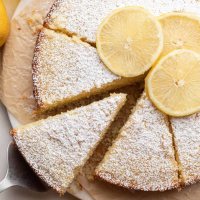 A sliced lemon olive oil cake on a piece of parchment paper. Once slice is being removed.