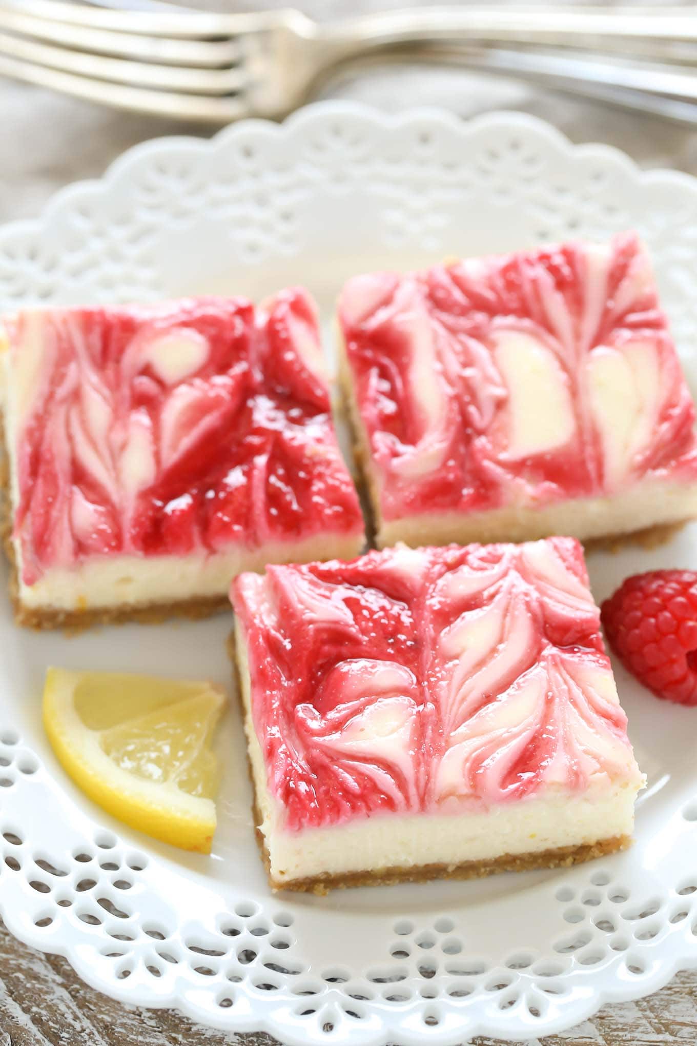 Three lemon raspberry cheesecake bars on a white dessert plate. 