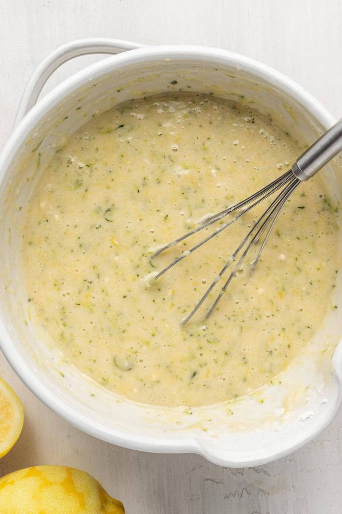 An overhead view of zucchini bread batter in a white mixing bowl, with a whisk.