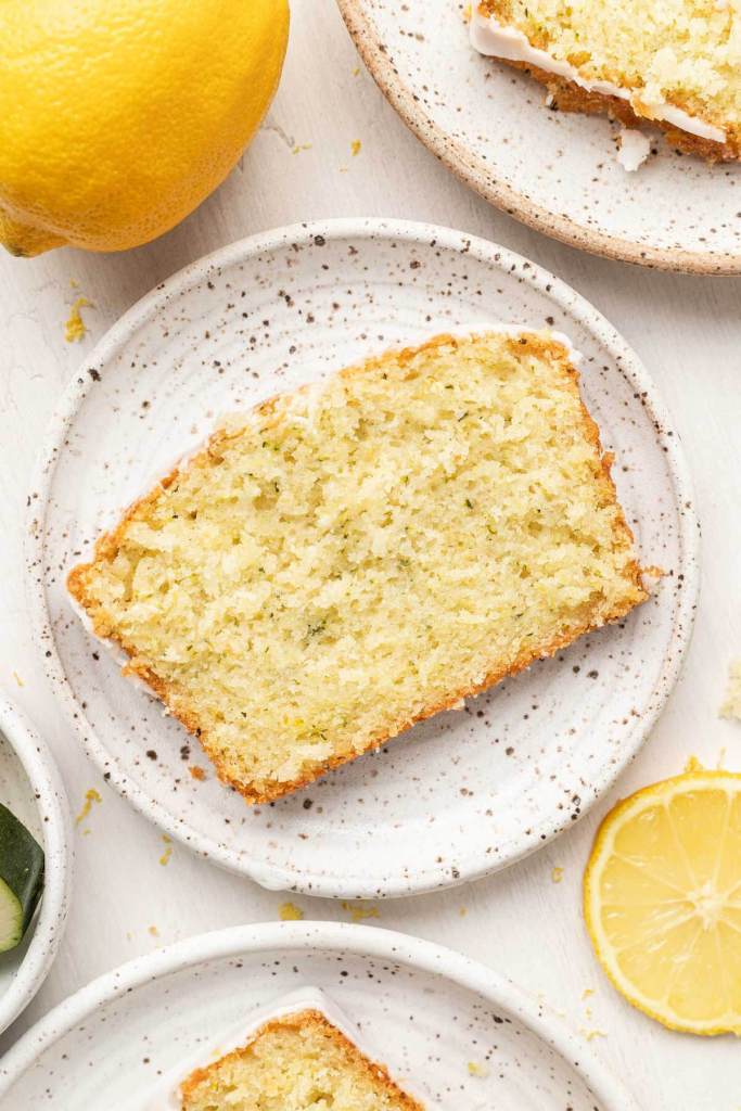 An overhead view of a slice of lemon zucchini bread on a speckled plate. 