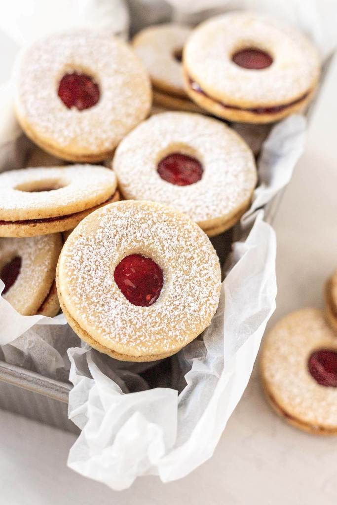 Classic Linzer cookies piled in a parchment paper-lined loaf pan. 