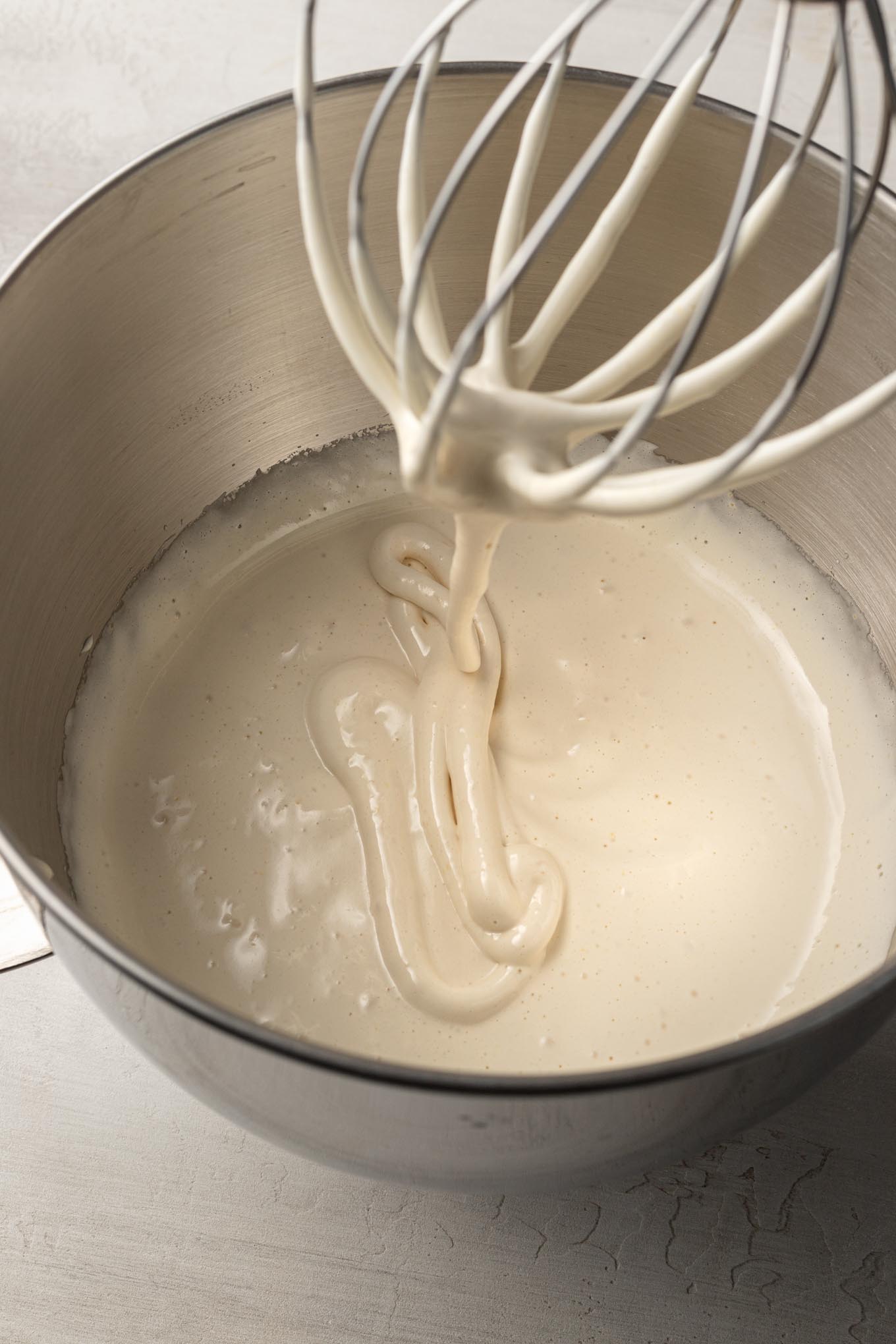 A beaten egg and sugar mixture in a mixing bowl with a whisk attachment.