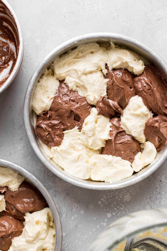 An overhead view of chocolate and vanilla cake batter dolloped into a round cake pan.