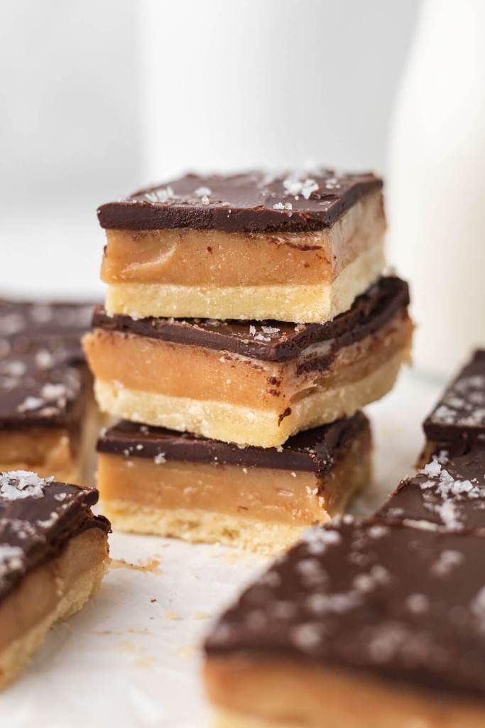 A stack of three millionaire shortbread bars, surrounded by additional bars. 