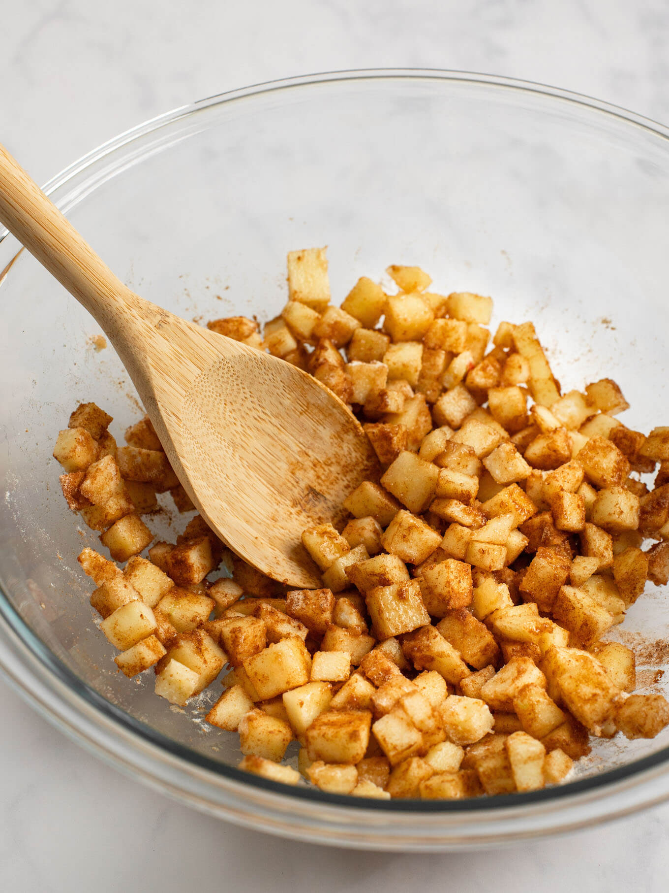 Apple pie filling mixed together in a glass mixing bowl with a wooden spoon.