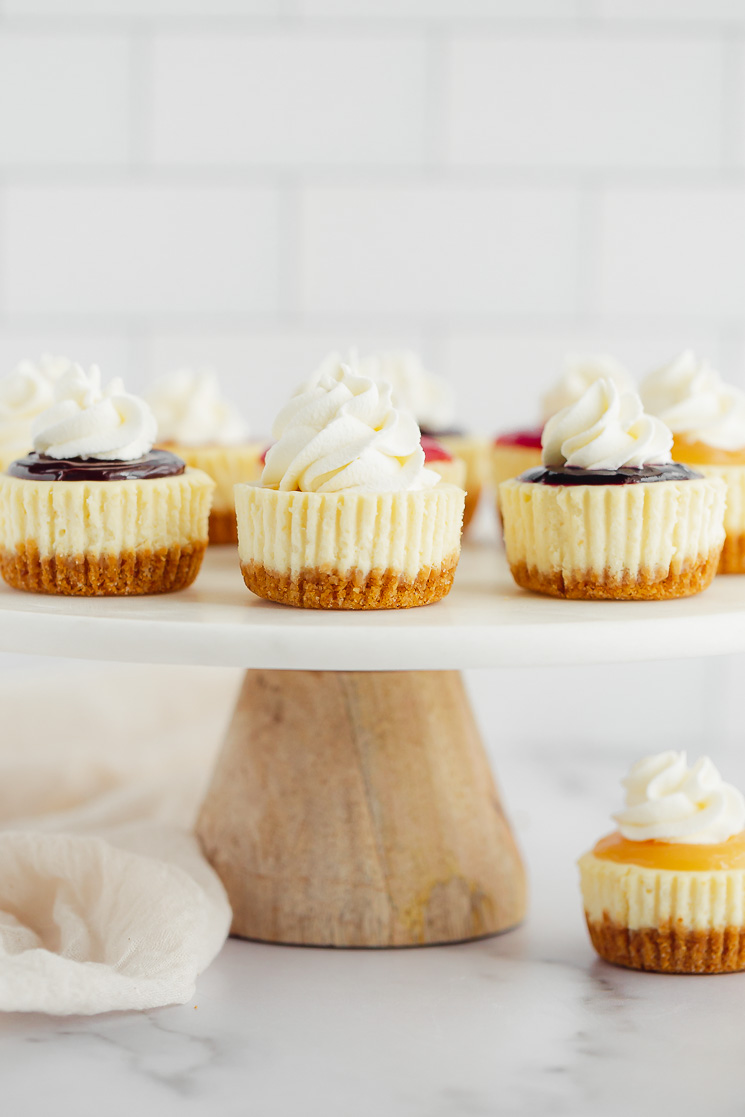 A marble cake stand displaying mini cheesecakes with multiple different toppings on them.