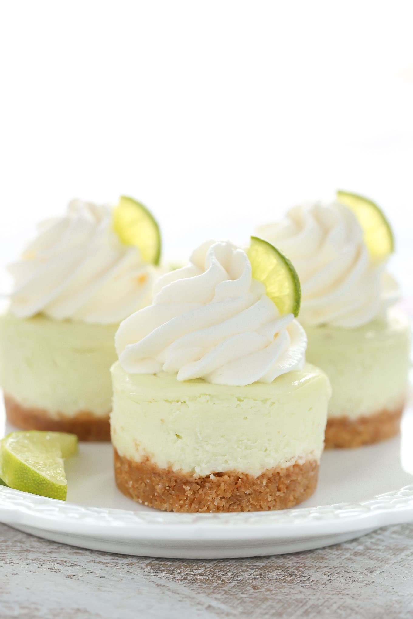 A side view of three key lime mini cheesecake bites on a white plate. 