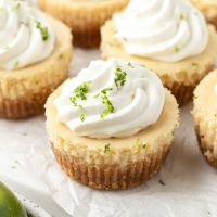 Mini key lime pies on a piece of parchment paper. Each mini pie is topped with whipped cream and a little lime zest.