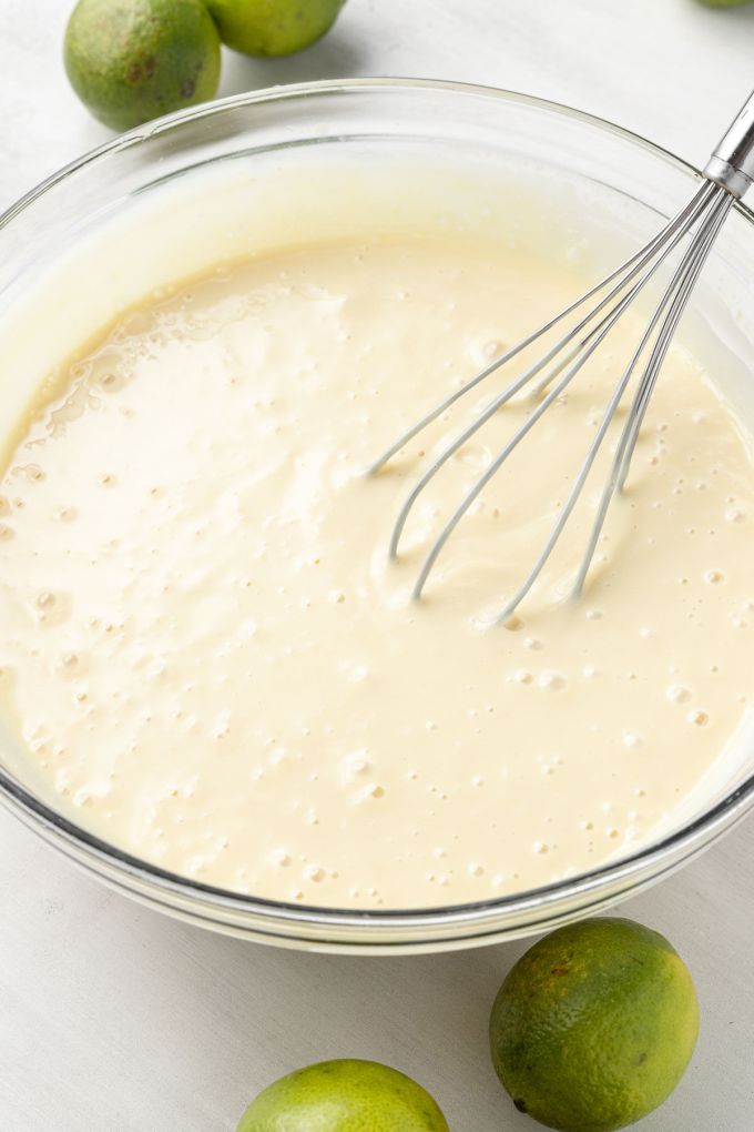 Key lime pie filling in a glass mixing bowl with a whisk.