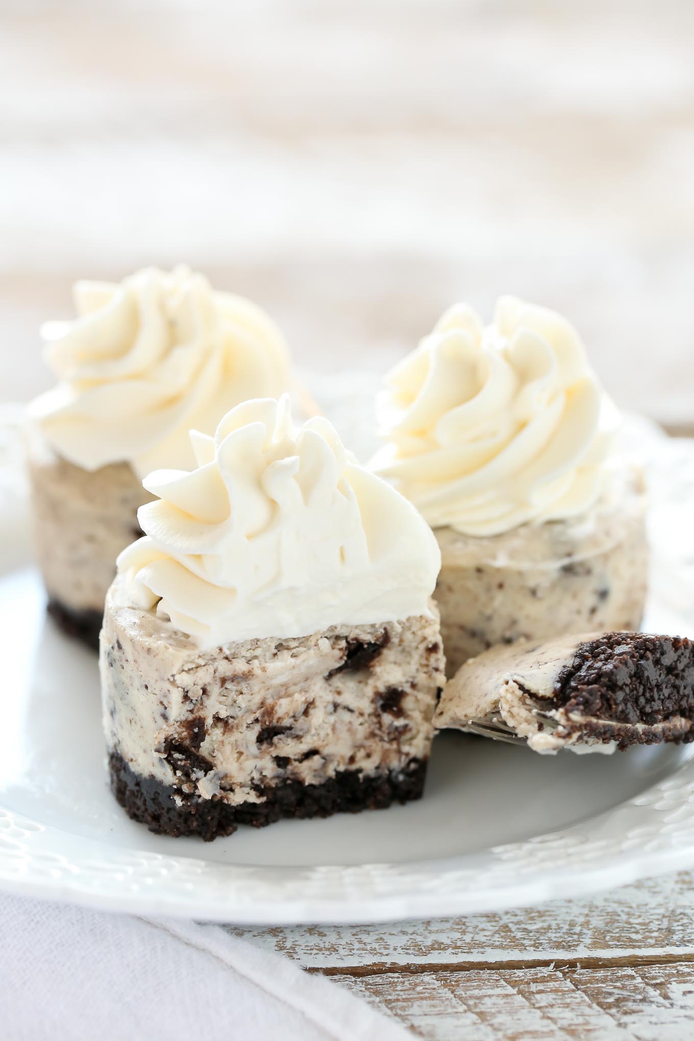 Three oreo cheesecake bites on a white plate. The front cheesecake has a bite missing. 