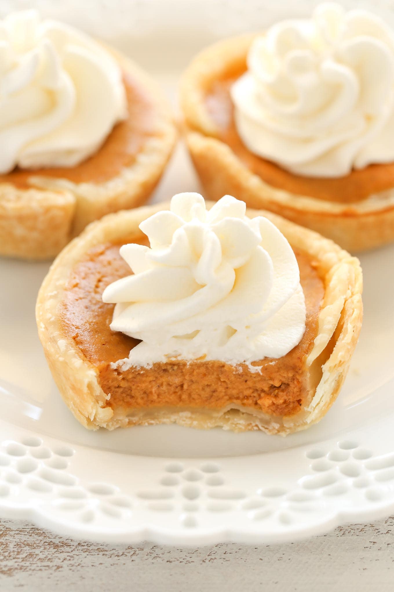 Three mini pumpkin pies topped with whipped cream on a decorative white plate.