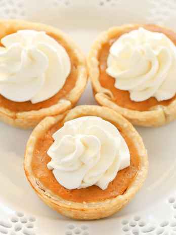 Three mini pumpkin pies topped with whipped cream on a decorative white plate.