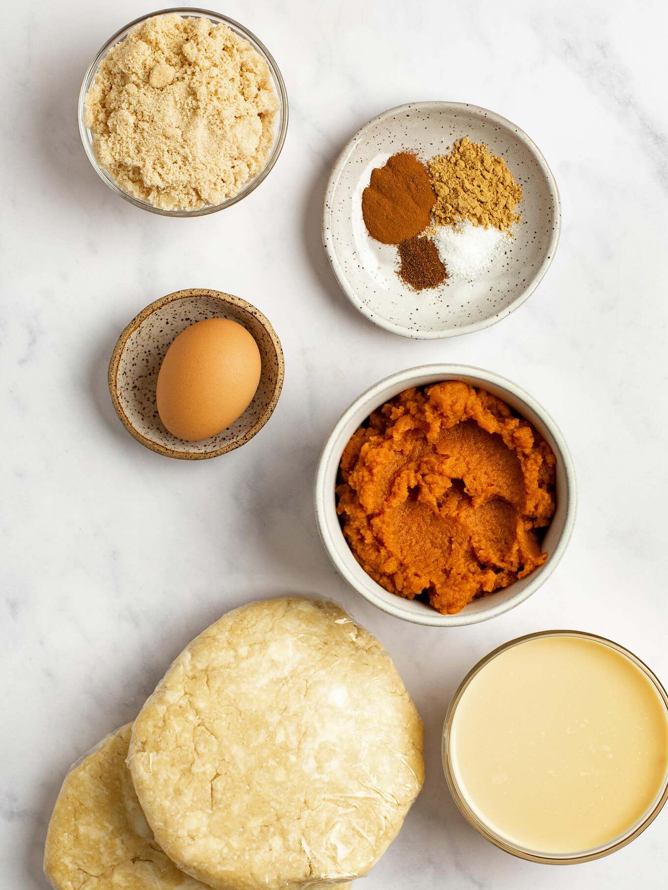 An overhead view of the ingredients for mini pumpkin pies on a marble surface.