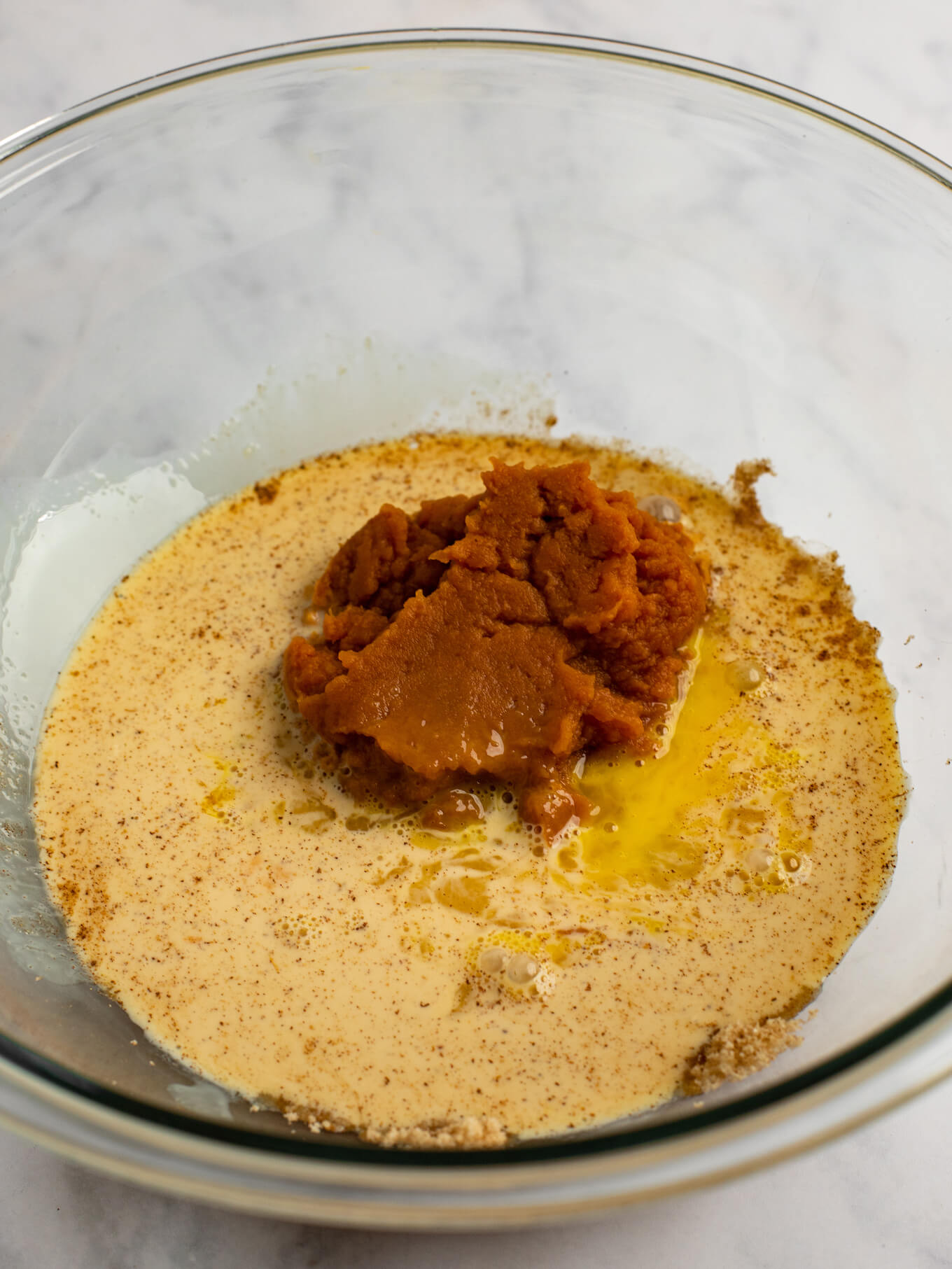 The ingredients for the pumpkin pie filling in a glass mixing bowl.